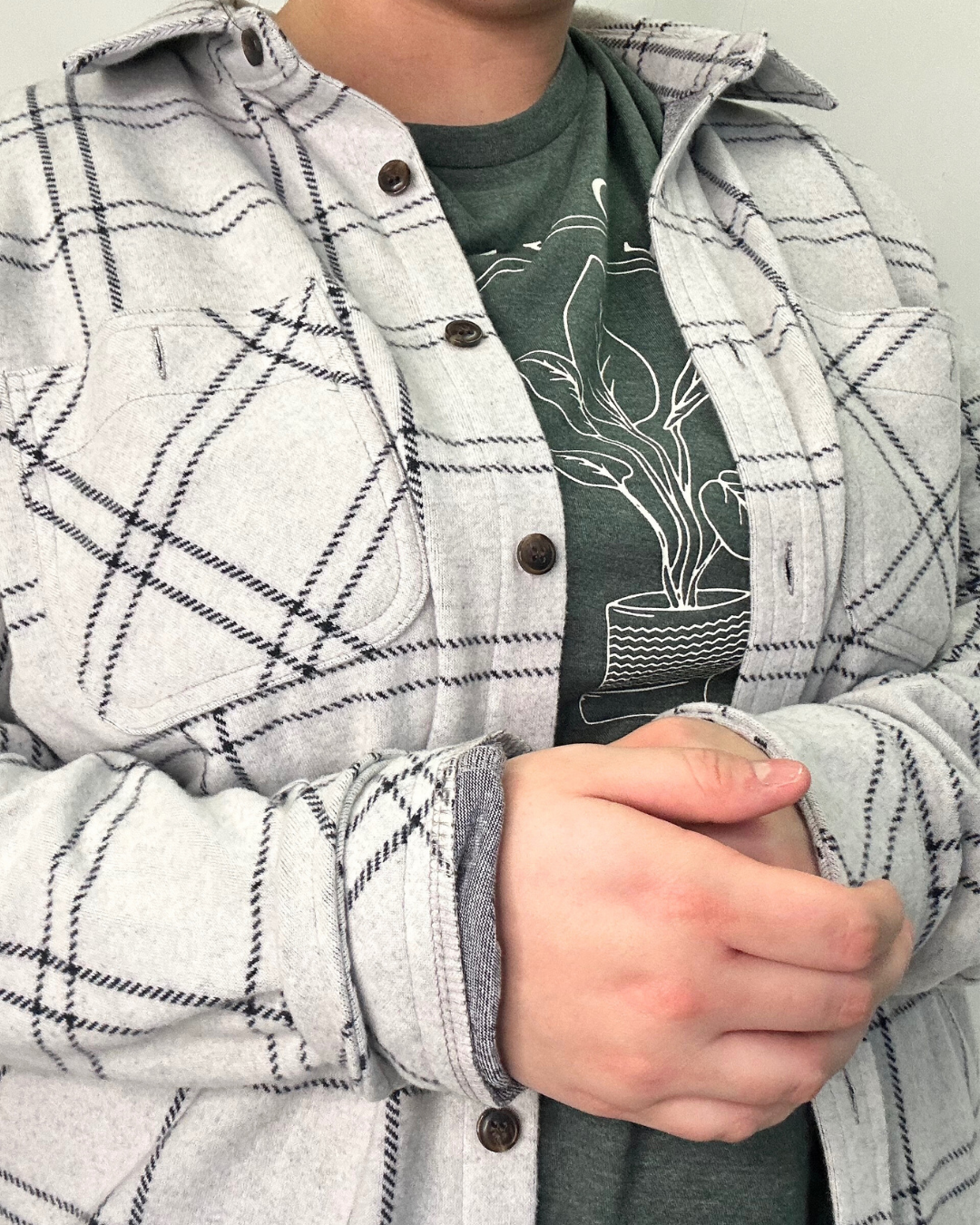 Person wearing a gray plaid shirt over a graphic t-shirt with plant design.